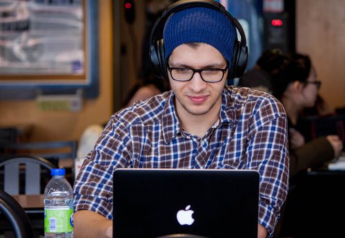 guy in plaid shirt and beanie, wearing headphones, working on a macbook
